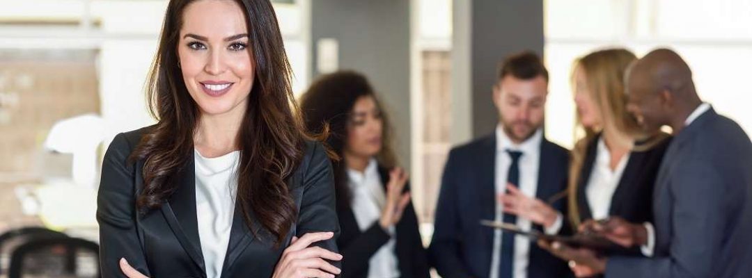 Businesswoman leader looking at camera in modern office with multi-ethnic businesspeople working at the background. Teamwork concept. Caucasian woman.